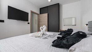 A modern hotel room with a large bed, a flat-screen TV, a bedside table, and a mirror. - Amazing home in Nedescina with sauna (Nedescina)