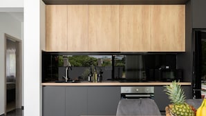 A modern kitchen with wooden cabinets, a black countertop, and a dining area with a table and chairs. - Amazing home in Nedescina with sauna (Nedescina)
