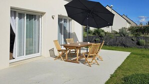 Un patio con tavolo e sedie, un ombrellone nero grande e una casa con pannelli solari.