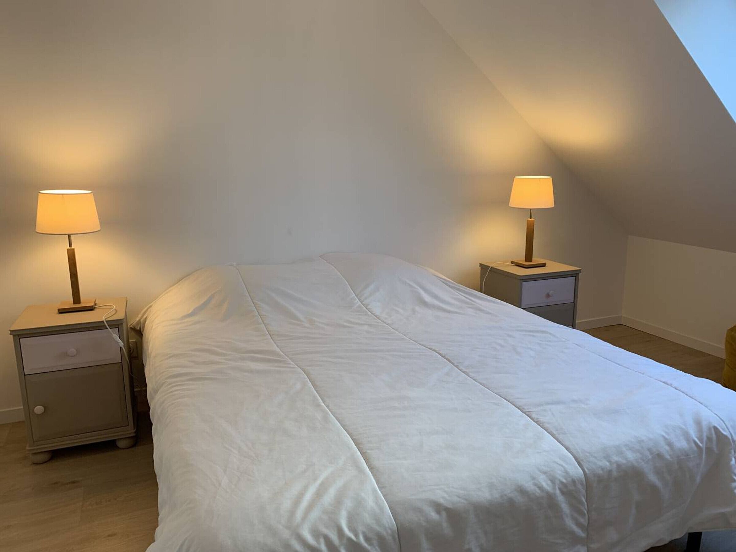 A bedroom with a bed, two bedside tables with lamps, and a sloped ceiling.