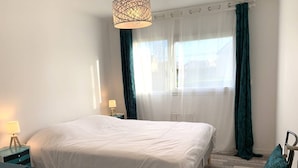 Una camera da letto con un letto, un comodino con una lampada, una sedia e una finestra con tende.