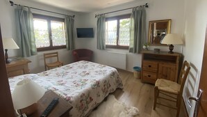 Ein Schlafzimmer mit Bett, Stuhl, Schminktisch, Spiegel und einem Fenster mit Vorhängen.