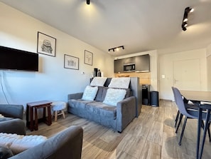 A modern living room with a grey sofa, a wooden coffee table, and a dining area with a table and chairs.