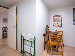 A room with a wooden table and chair, a green metal rack, a white door, and a bulletin board with various notices. - Seaside Apartment with Pool and Private Parking (Torredembarra)