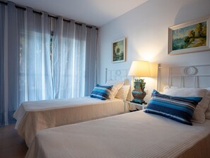 A hotel room with two beds, a nightstand with a lamp, and a painting on the wall. - Seaside Apartment with Pool and Private Parking (Torredembarra)