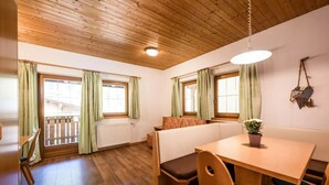 Une pièce avec un plafond en bois, une table à manger en bois entourée de chaises, un banc et une fenêtre avec des rideaux.