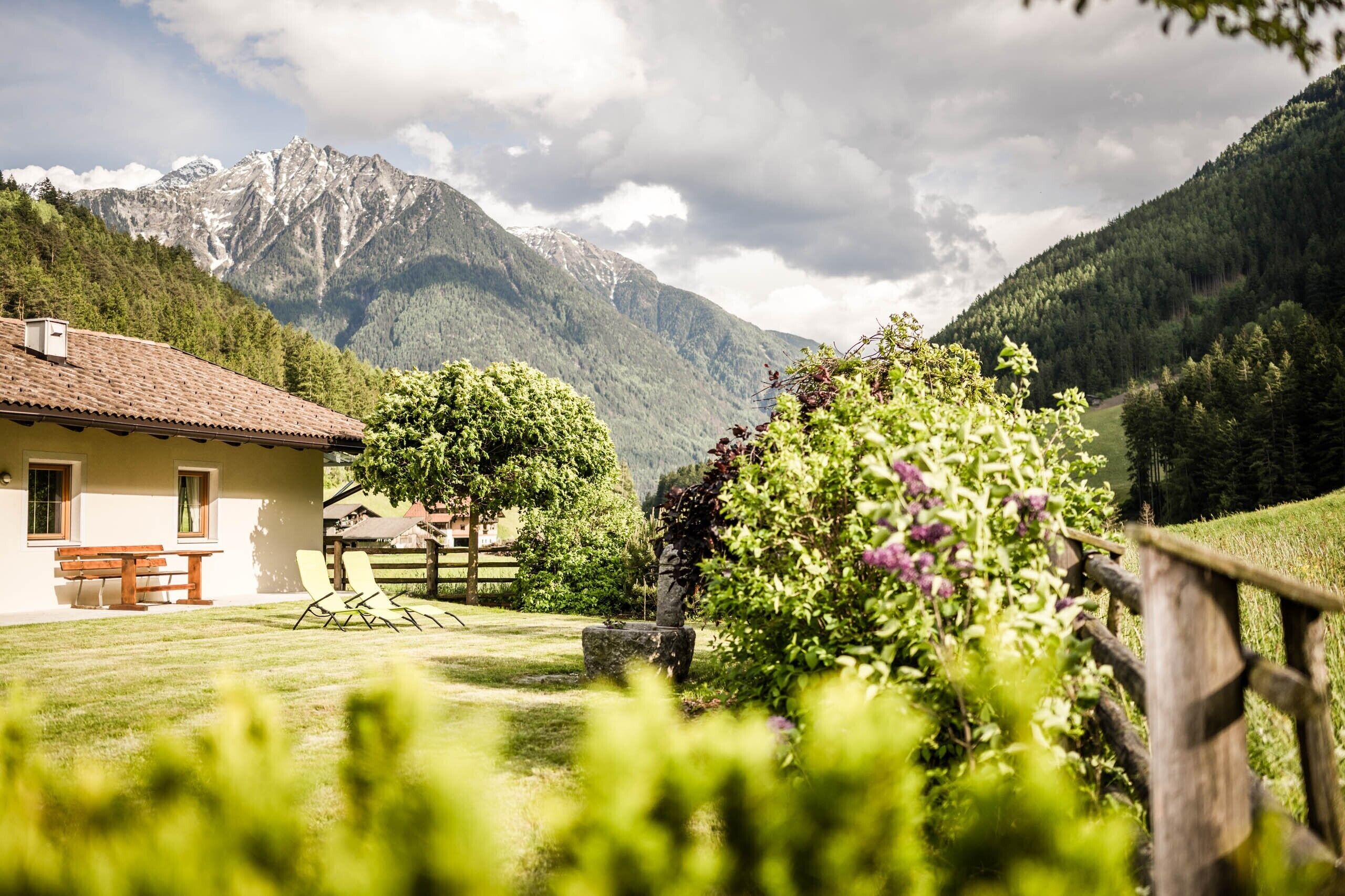 Una casa con patio, valla de madera y montañas al fondo.