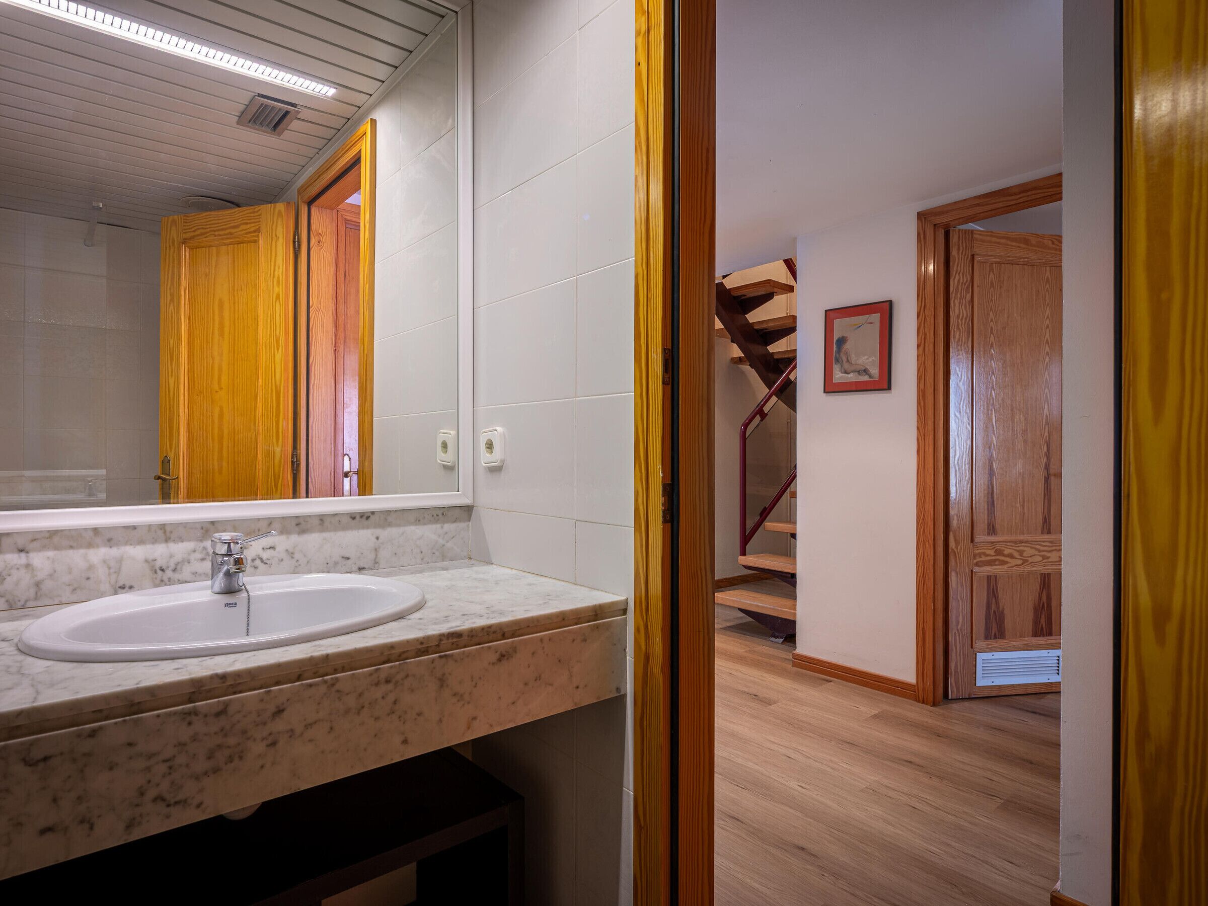 A bathroom with a marble sink, wooden door, and a staircase leading to another room.