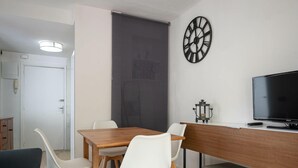 Ein modernes Wohnzimmer mit einem Holzesstisch, weißen Stühlen, einem Fernseher und einer Wanduhr.