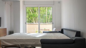Ein modernes Hotelzimmer mit Bett, Stuhl, Tisch und Blick auf Bäume durch eine Glastür.