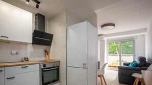 Eine moderne Küche mit weißen Schränken, einem eingebauten Ofen und einem großen Kühlschrank. Ein Holzarbeitsplatz und ein Fenster sorgen für natürliches Licht.