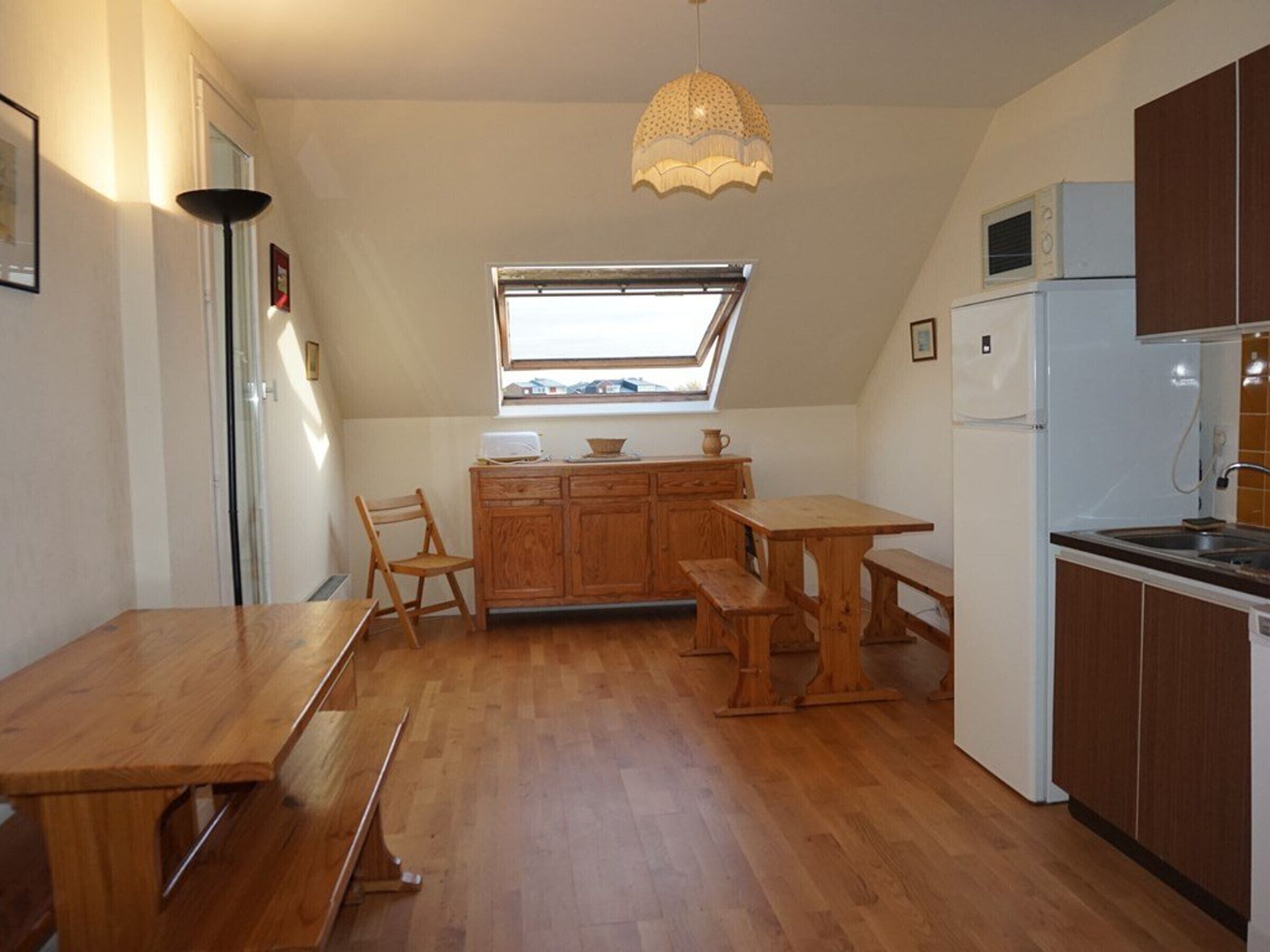 Cocina compacta con armarios de madera, una mesa de comedor y un banco. Hay una ventana sobre el fregadero y una lámpara en el techo.