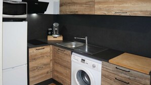 Een compacte keuken met een ingebouwde wasmachine, koffiezetapparaat en magnetron.