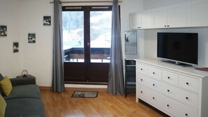 Een woonkamer met een bank, een televisie, een kast en een raam met gordijnen.