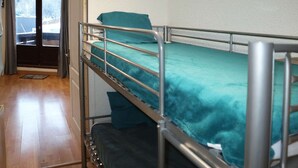 Een stapelbed met een blauwgroene matras in een kamer met houten vloeren en een deur naar buiten.