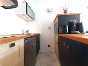 Ett kompakt kök med diskmaskin, mikrovågsugn, kaffebryggare och ett litet handfat.