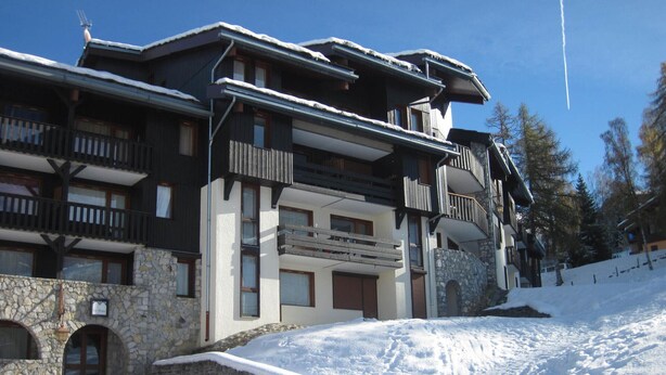 A multi-story hotel with balconies, stone facade, and a ski slope in the background.