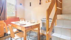 A dining area with a wooden table and chairs, a staircase, and a view of the outdoors.