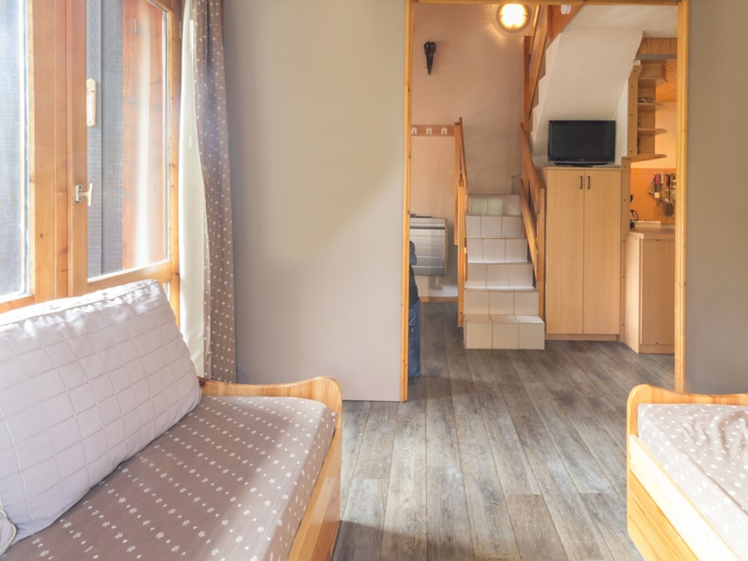 A cozy room with a bed, a small desk, and a staircase leading to a kitchen area.