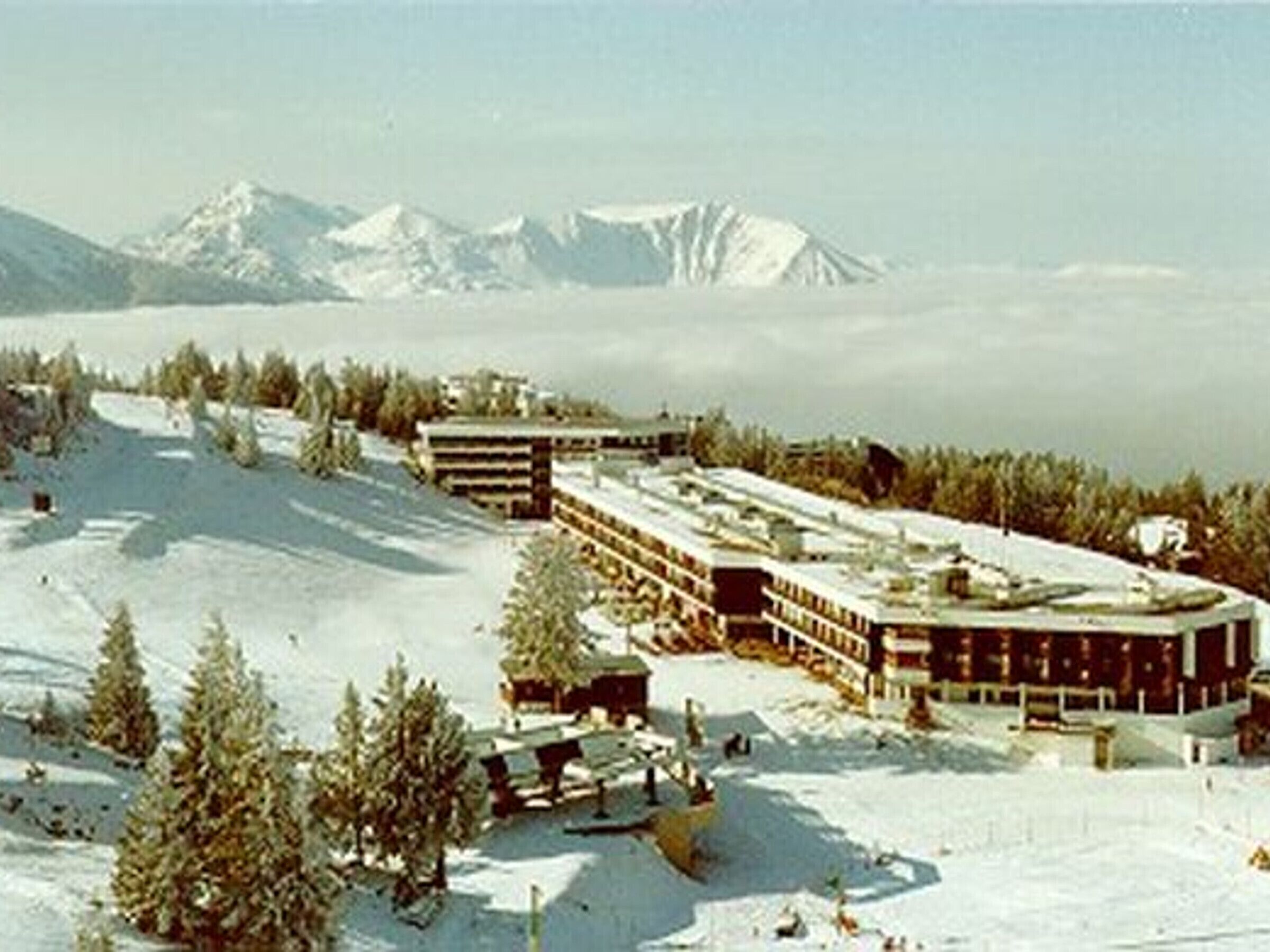 A snow-covered hotel with multiple buildings, surrounded by trees and mountains in the background.