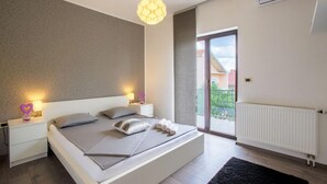 Una camera da letto moderna con un letto grande, lampade ai comodini, vista su un balcone esterno tramite una porta scorrevole e un termosifone sulla parete.