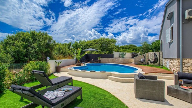 Un giardino sul retro con piscina, poltrone relax e un muro in pietra.