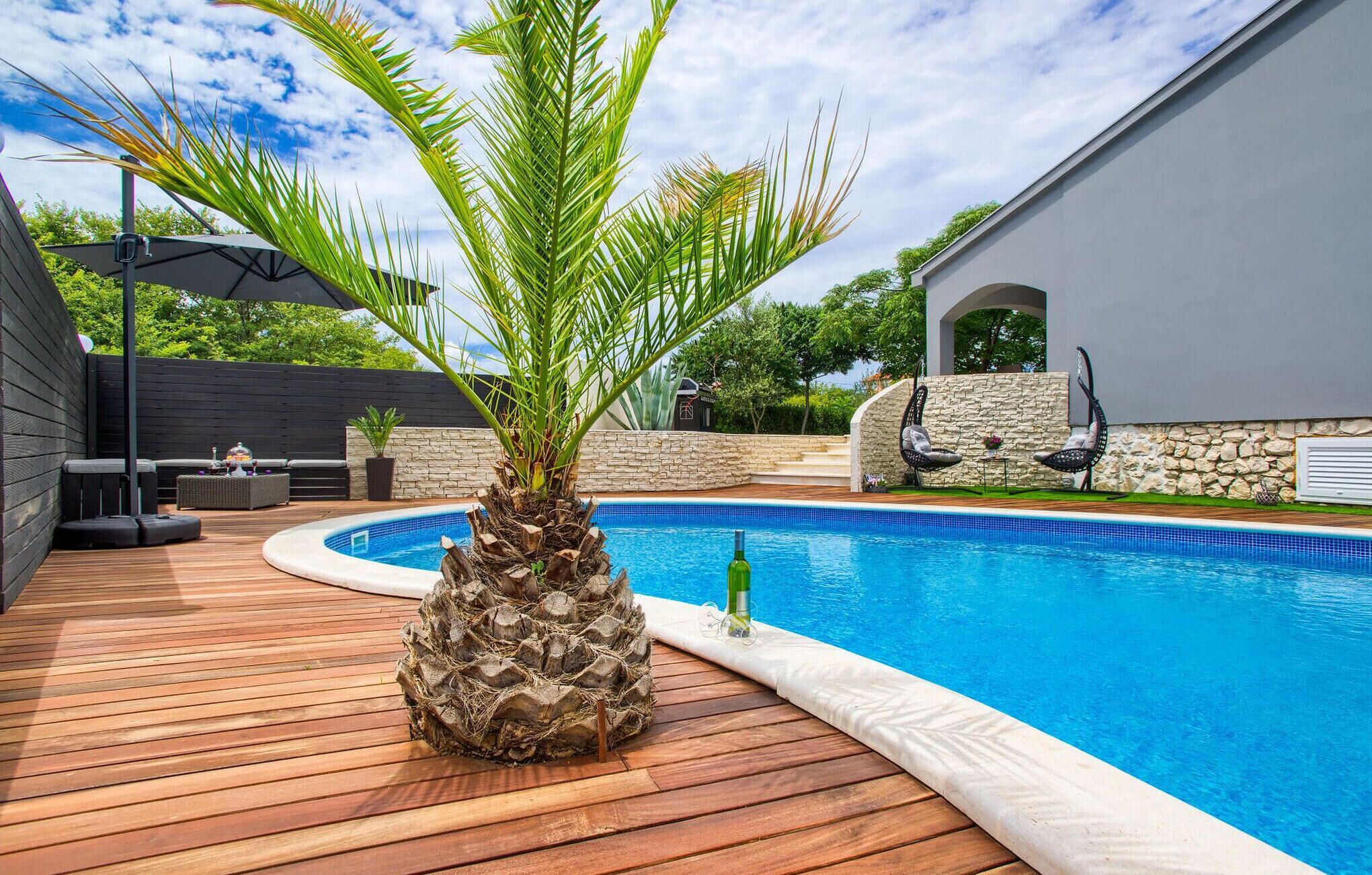 Zwembad met houten terras, een palmboom en tuinmeubilair.