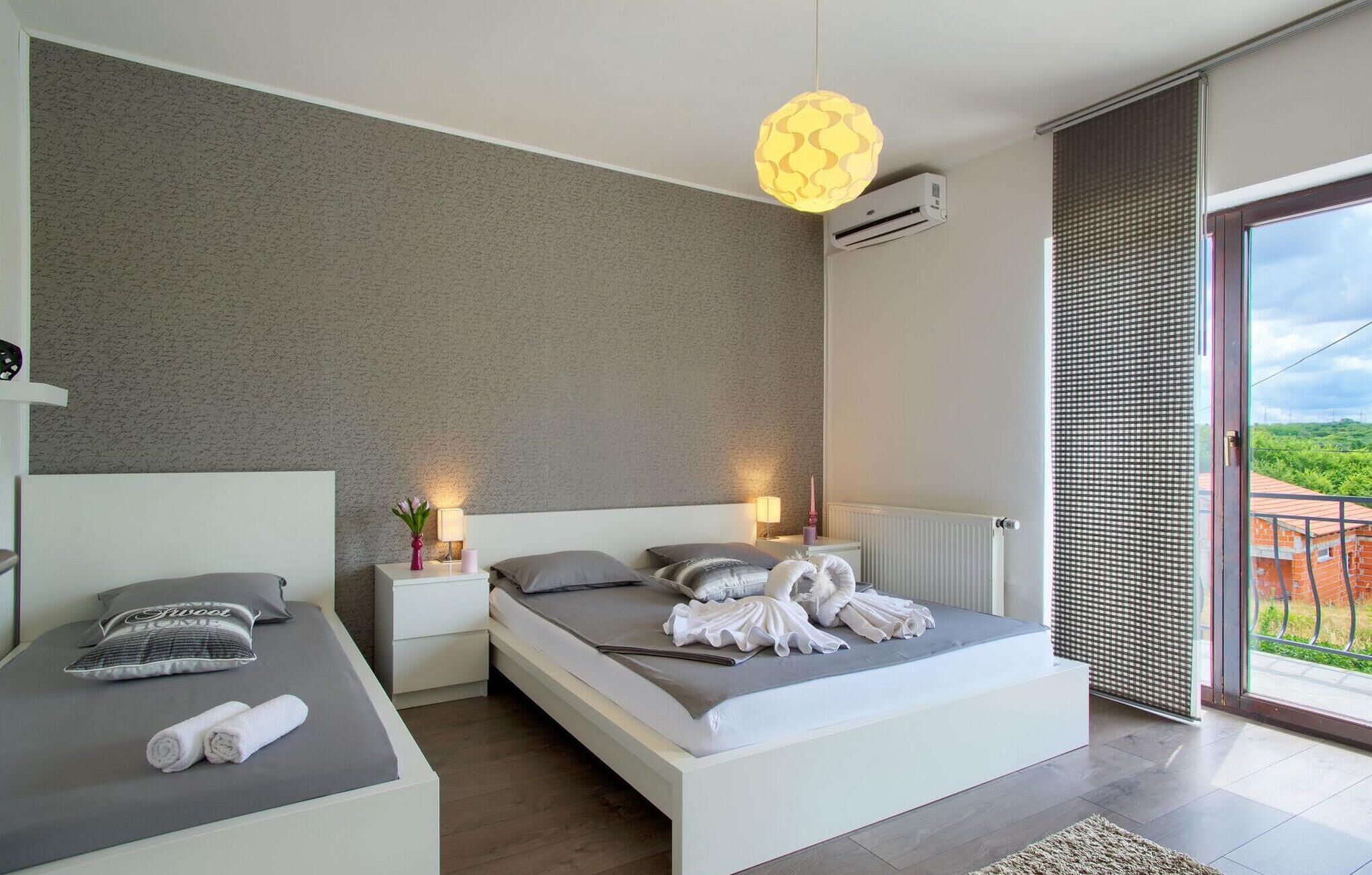 Un dormitorio moderno con una cama grande, mesitas de noche, una lámpara colgante y vistas a la vegetación a través de la ventana.