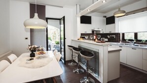Una cucina moderna con mobili bianchi, un'isola centrale con sgabelli da bar, illuminazione a sospensione e vista all'esterno.