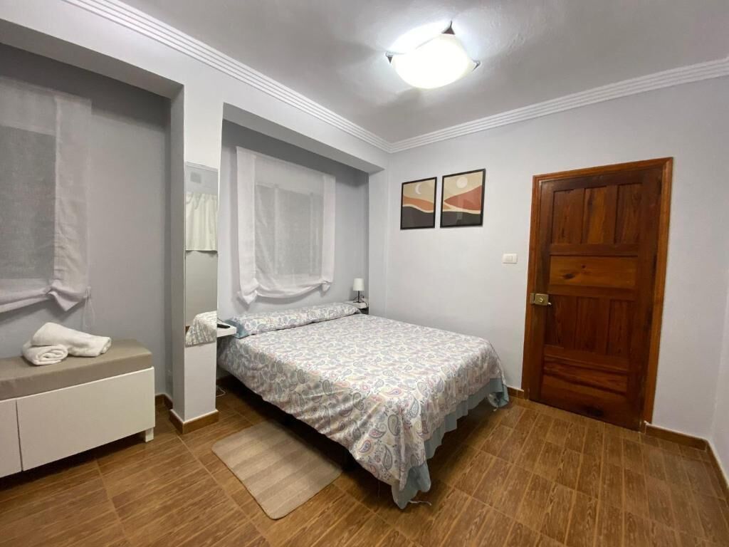 Ein Schlafzimmer mit einem Bett, einem Nachttisch, einem Spiegel, einer Holztür und zwei an der Wand hängenden Bildern.