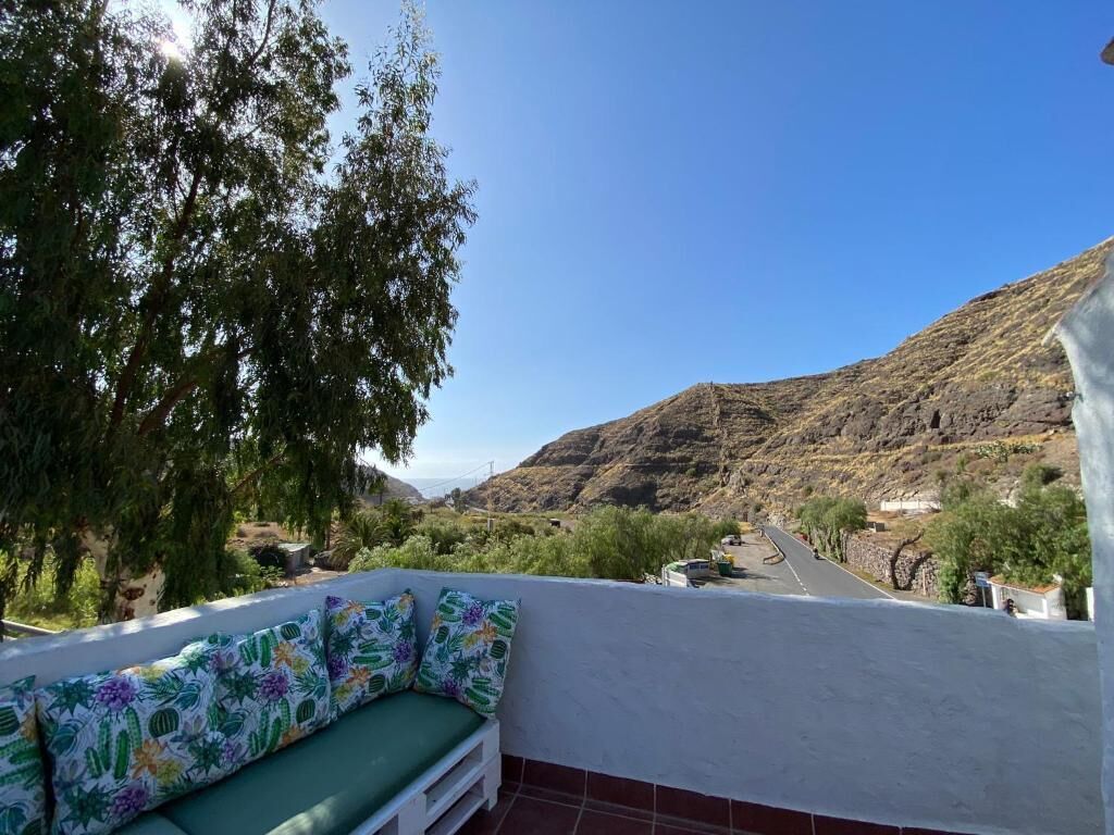 Un balcón con un banco acolchado verde y vistas a una carretera que serpentea hacia una zona montañosa.