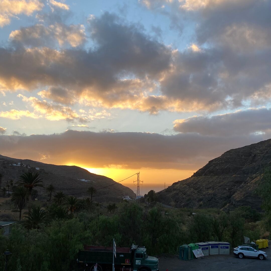 Ein Sonnenuntergang über einer hügeligen Landschaft mit einer Straße, einem Lastwagen und Gebäuden im Vordergrund.