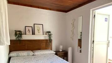 Une chambre avec un plafond en bois, un lit recouvert d’une couvre-lit à motifs floraux, une table de chevet, un miroir fixé au mur et une porte ornée du symbole du Wi-Fi.