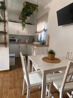 A kitchen with white cabinets, a microwave, and a sink. There is a dining table with chairs and a plant on it. - Alojamientos Charco Azul (Agaete)