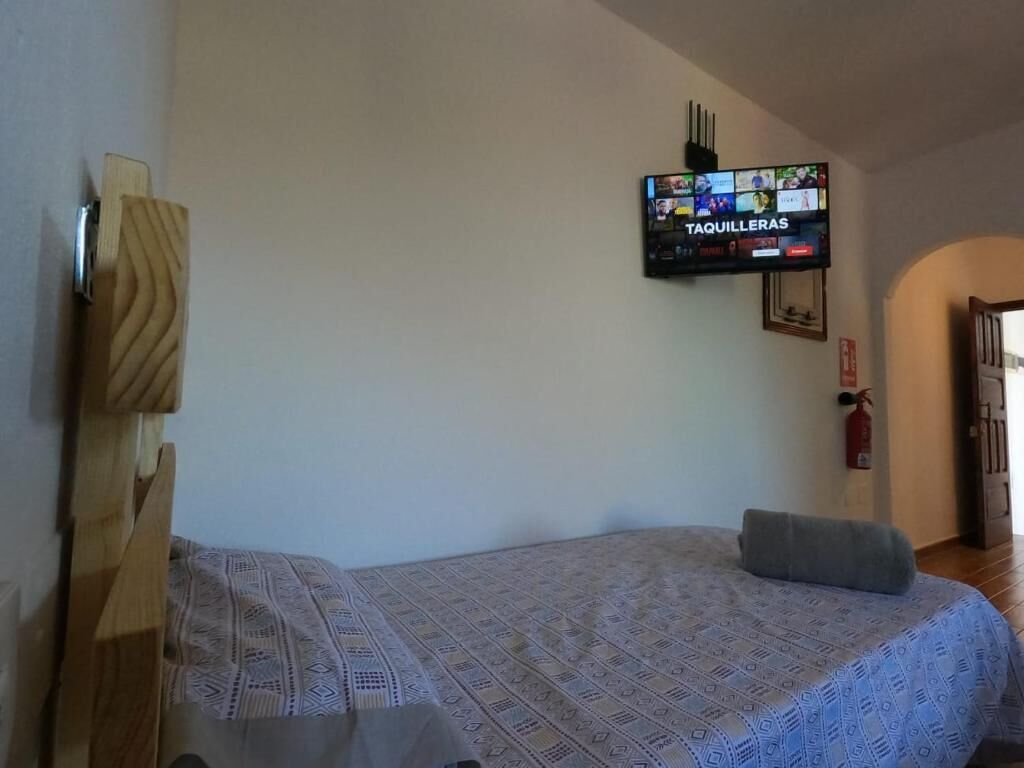 A bedroom with a bed, a television mounted on the wall, and a wooden headboard.