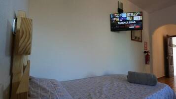 A bedroom with a bed, a television mounted on the wall, and a wooden headboard.