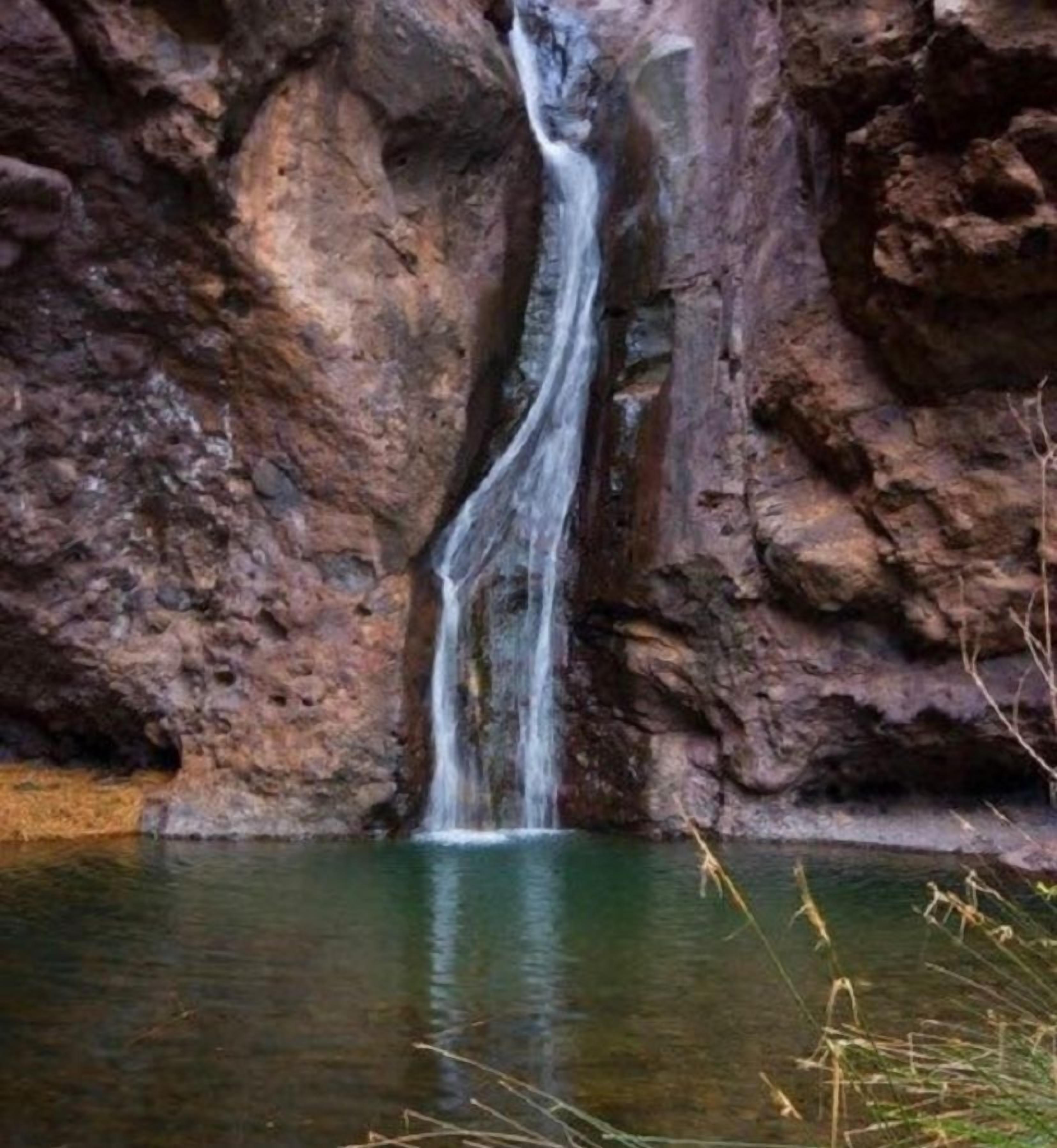 Una cascada se precipita desde un risco rocoso hacia una masa de agua.