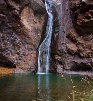 A waterfall cascading down a rocky cliff into a body of water. - Alojamientos Charco Azul (Agaete)