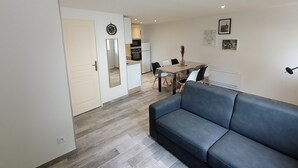 A modern living room with a grey sofa, a dining area with a table and chairs, and a kitchen in the background. - 6 Personnes / Proche Disney et Aéroport CDG (Annet-sur-Marne)