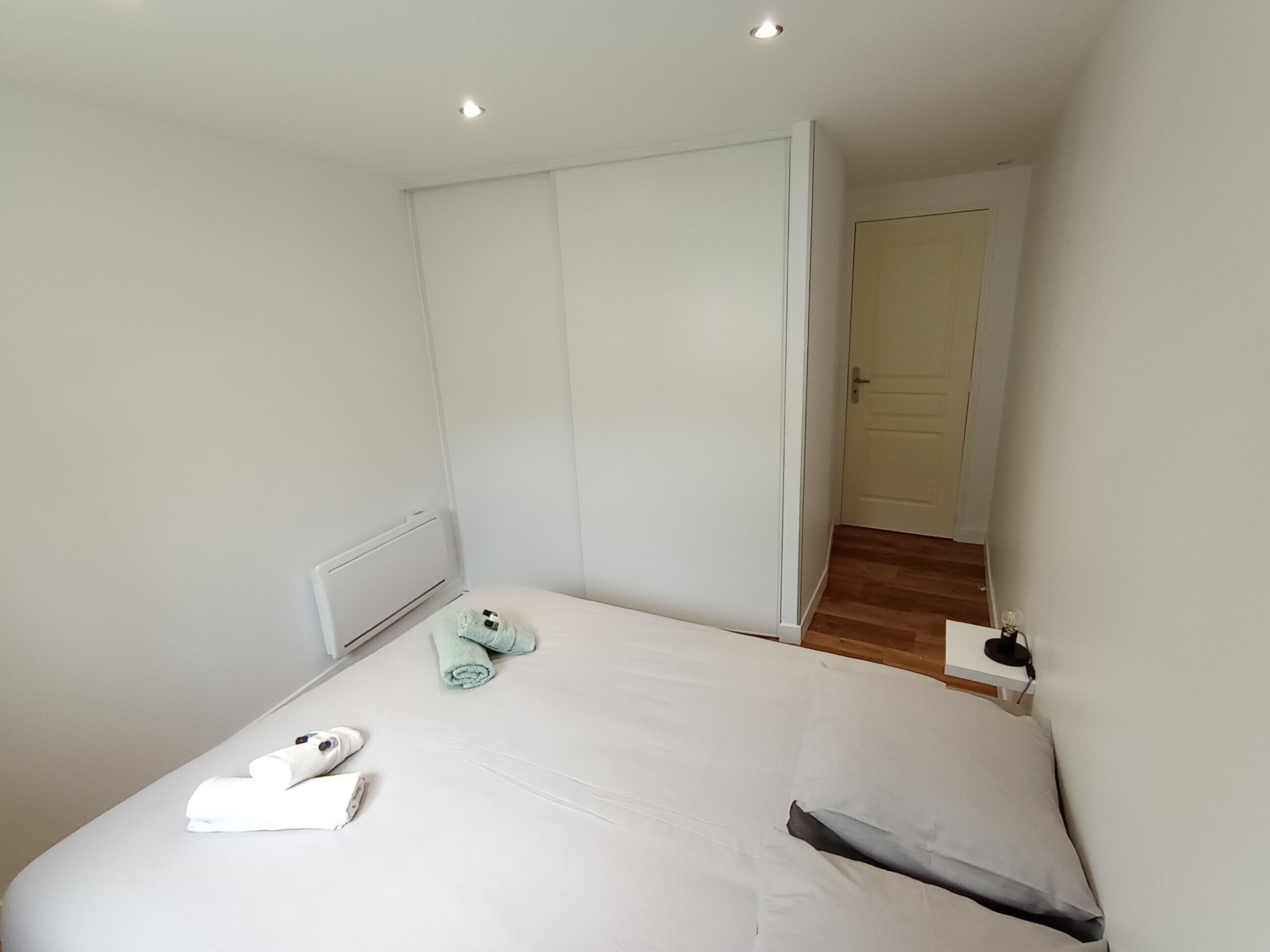 Un dormitorio con cama, un radiador, una toalla y un par de zapatos.