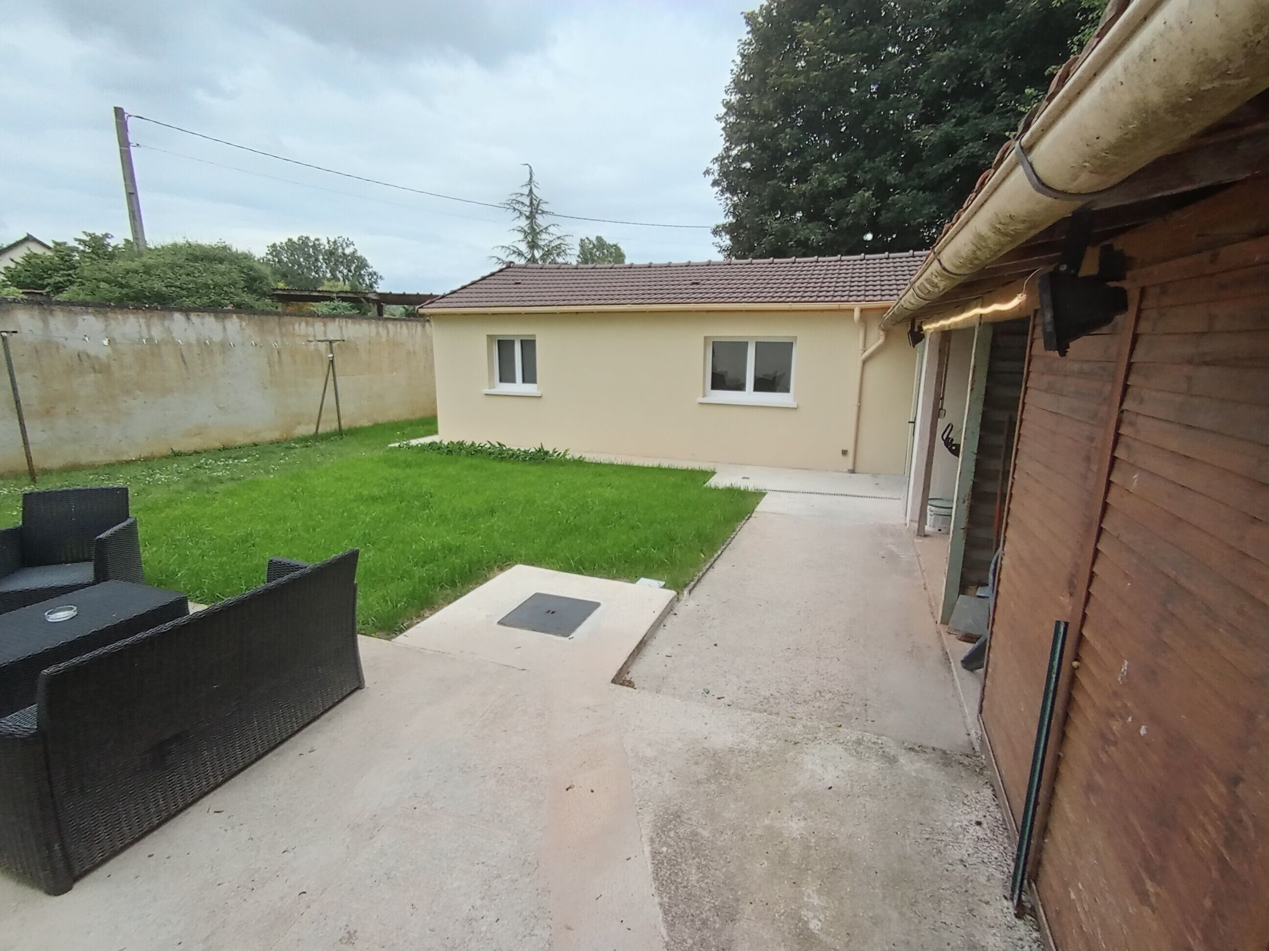 Un jardin avec une terrasse, une petite pelouse et une clôture en bois.