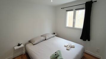Een minimalistische slaapkamer met een groot bed, een raam met gordijnen en een klein nachtkastje.