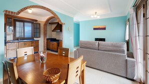 A dining area with a wooden table, chairs, and a basket. There is a kitchen with a brick archway and a sofa in the living area. - Holiday Home 'Casa Girdana' with Sea View, Private Terrace and Wi-Fi (Valverde)