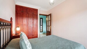 A bedroom with a bed, wooden wardrobe, and a nightstand with a lamp. - Holiday Home 'Casa Girdana' with Sea View, Private Terrace and Wi-Fi (Valverde)