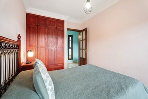 A bedroom with a bed, wooden wardrobe, and a nightstand with a lamp.