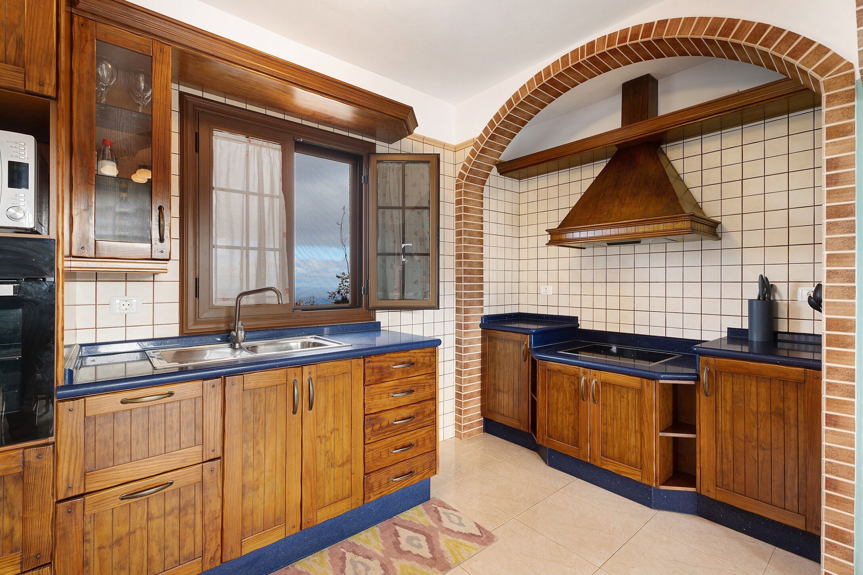 Una cocina con armarios de madera, horno empotrado y salpicadero de azulejos.