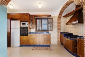 A kitchen with wooden cabinets, a white refrigerator, a microwave, a sink, and a window with curtains.