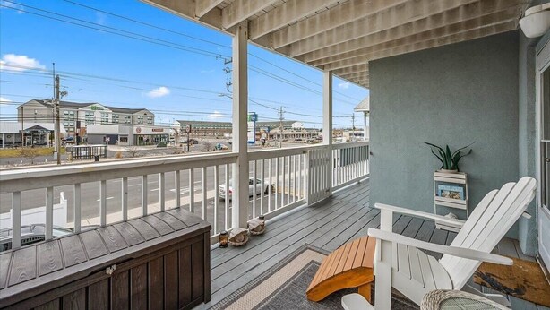 A covered porch with a view of the street, white chairs, and a small table. - Nicely Renovated Two Bedroom Oceanside Condo (Ocean City)