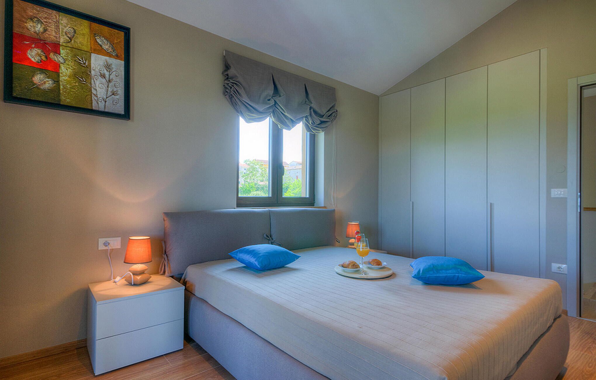 Une chambre à coucher avec un lit, des tables de chevet, une fenêtre avec des rideaux et un tableau au mur.