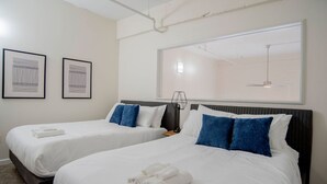 A hotel room with two beds, white bedding, blue pillows, a large window, and two framed artworks on the wall. - 3BR CozySuites TheBlock Skybridge Access (Indianapolis)
